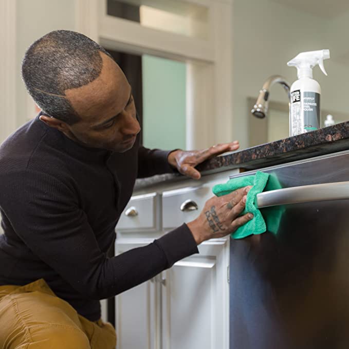 A man cleaning a kitchen with a green cloth.