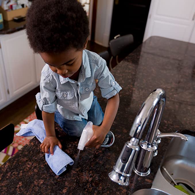 A young boy cleaning a kitchen counter.